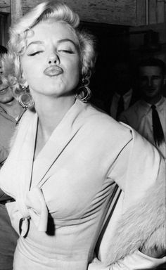 black and white photograph of marilyn monroe blowing out her tongue with other people in the background