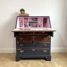 an old fashioned desk with pink and blue drawers on it's top, in front of a white wall