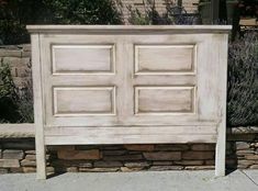 an old white wooden bed frame sitting on the side of a sidewalk next to a brick wall