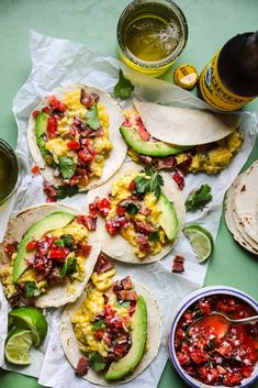 breakfast tacos with eggs, avocado and salsa on paper next to beer