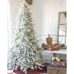 a white christmas tree sitting on top of a wooden floor next to a mirror and suitcase