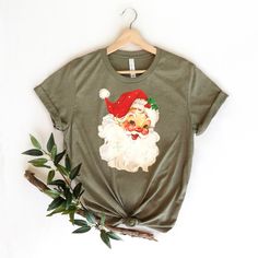 "Cute Santa Face Shirt, Vintage Santa Claus T-Shirt, Christmas Santa Shirt, Christmas T-Shirt, Funny Christmas Tee, Cute Santa Tee, Xmas Tee ☀️☀️☀️☀️☀️ Everything in our shop is hand crafted and made to order. If you want different color or size contact me! If you would like something custom made to fit your personal style please message me and I will do everything to get you that something special. ---How To Order--- ⭐️Please, check and review all photos ⭐️Choose your t-shirt size and color ⭐️Enter your Design Color Example: \"White\" ⭐️Click add to cart. You can go back to add more product ⭐️Click \"Proceed to check out\" ⭐️When you check out, you can add a note to seller for any request *High quality and super soft, comfortable shirt. Made with top of the line vinyl and pressed with a p Funny Print Christmas T-shirt, Christmas Funny Print Short Sleeve T-shirt, Festive Christmas Crew Neck T-shirt, Christmas Graphic Tee With Short Sleeves, Christmas Holiday T-shirt With Short Sleeves, Christmas Cotton T-shirt With Funny Print, Christmas Crew Neck Shirt Gift, Christmas Graphic Tee Shirt For Holiday, Christmas Gift Crew Neck Shirt