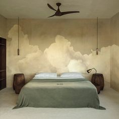 a large bed sitting under a ceiling fan in a room with clouds painted on the wall