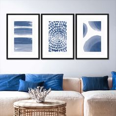 three blue and white paintings hang on the wall above a couch in a living room