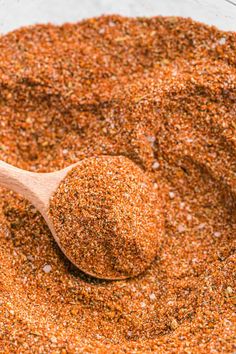 a wooden spoon in a bowl filled with ground chili powder and seasoning flakes