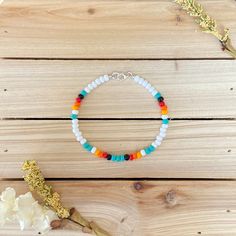 a bracelet with multicolored beads sits on a wooden table next to a flower