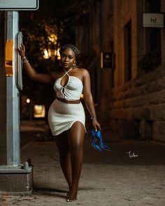 a woman in a white dress leaning against a street sign with her hand on the pole