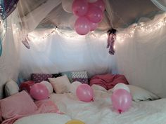 balloons are floating in the air above a bed with white sheets and pink pillows on it