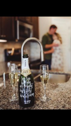 a bottle of wine and two glasses on a kitchen counter with a couple in the background