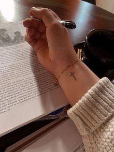 a person with a cross tattoo on their wrist is holding a pen and looking at an open book