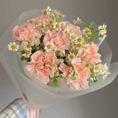 pink carnations and daisies are arranged in a white paper wrapper on top of a plaid napkin