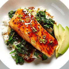 a white plate topped with salmon and rice next to an avocado slice on top of it