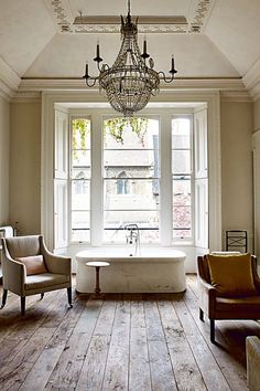 a chandelier hangs from the ceiling over a bathtub in front of two windows