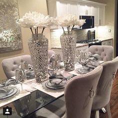 a dining room table set for four with white flowers in vases on the center