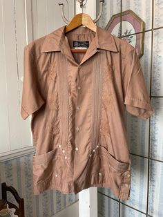 This gorgeous shirt was made in Mexico from a light, silky feeling blend of 80 per cent polyester and 20 per cent cotton in dark beige/light brown. The front is decorated with decorative stitching, embroidered designs and lots of buttons! The shirt has two front pockets. Marked size large/40. The measurements, taken with the shirt lying flat, are: shoulder to shoulder, 19 inches; armpit to armpit, 23 inches; sleeves, 10 inches; length, 30 1/2 inches; bottom edge, 26 inches. In very good condition. Beige Short Sleeve Camp Shirt For Beach, Brown Short Sleeve Camp Shirt With Pockets, Brown Collared Camp Shirt For Summer, Brown Camp Shirt With Pockets For Summer, Brown Button-up Camp Shirt For Summer, Summer Brown Button-up Camp Shirt, Brown Collared Beach Shirt, Brown Short Sleeve Collared Shirt For Summer, Brown Collared Short Sleeve Shirt For Summer