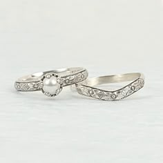 two wedding rings are shown on a white surface with one ring has a pearl in the middle