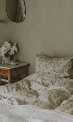 an unmade bed with white sheets and flowers on the side table in front of it