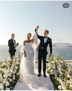 a bride and groom holding their hands up in the air as they walk down an aisle with white flowers