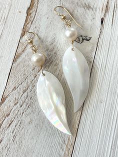 "Luminous White mother of Pearl earrings, hand carved Maile leaf with 14 kt gold fill or sterling silver and white freshwater pearl. hangs about 1 7/8\" down from ear wire and 1/2\" wide.  For centuries, leis made from the shiny fragrant leaves of maile (alyxia oliviformis) have been used to communicate love, respect, blessing, enduring devotion, reverence, friendship, and a desire for peace. Maile is an indigenous vine or shrub found in wet forests throughout the Hawaiian Islands." Handmade White Leaf-shaped Jewelry, Mother Of Pearl Earrings, White Freshwater Pearl, Hawaiian Islands, Leaf Earrings, Ear Wire, Mother Of Pearl, Fresh Water, Freshwater Pearls