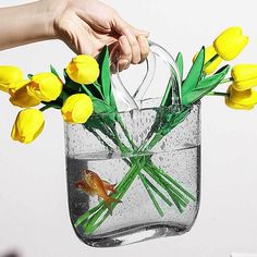 a person holding a vase with yellow flowers in it and a goldfish swimming inside