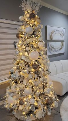 a white christmas tree with gold and silver ornaments on it's branches in a living room