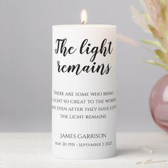 a white candle with the words'the light remains'printed on it next to a pink vase