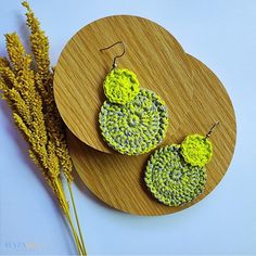 two crocheted earrings sitting on top of a wooden plate next to a plant