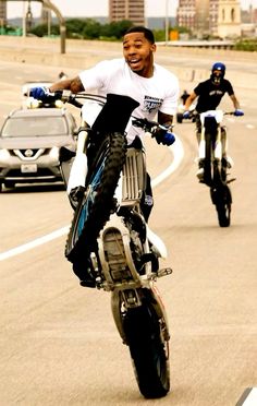 two men riding motorcycles on the road with cars in the backgrouds behind them