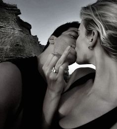 a man and woman kissing each other in front of a rock face by the ocean