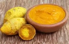 a bowl filled with yellow liquid next to two pieces of ginger