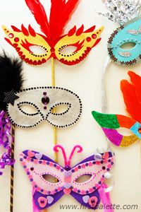 masquerade masks are lined up on a white surface with feathers and beads around them