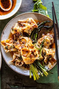 a plate filled with dumplings and vegetables next to chopsticks on a table