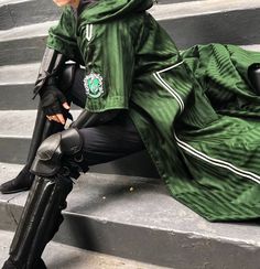 a woman sitting on the steps wearing black boots and a green coat with white stripes