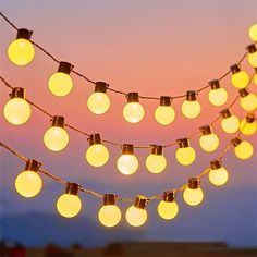 a string of light bulbs hanging from the side of a building at dusk with mountains in the background