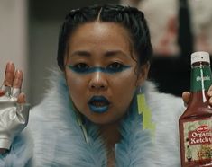 a woman with blue makeup holding a bottle of ketchup and an object in her hand