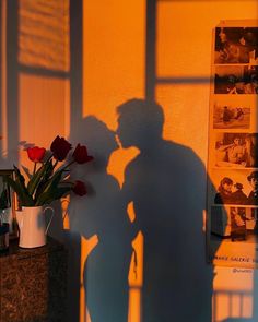 the shadow of a man and woman kissing in front of a wall with pictures on it