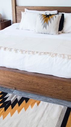 a bed with white sheets and pillows on top of it next to a wooden headboard