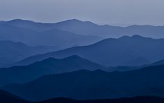 the mountains are covered in blue hues as seen from an airplane on a cloudy day