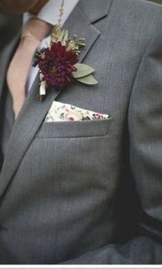 a man wearing a gray suit with a red flower on the lapel and pocket square