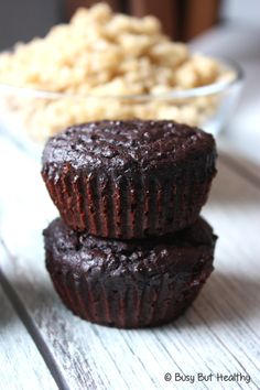 two chocolate muffins sitting on top of a wooden table next to a bowl of oatmeal