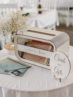 a white table topped with a card box next to a vase filled with baby's breath flowers