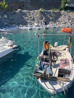 two boats are in the water near some rocks and sand, with one boat sitting on it's side