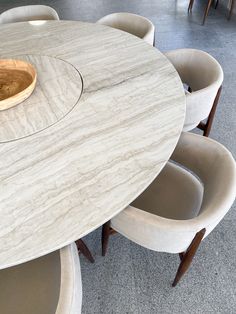 a marble dining table surrounded by chairs and a wooden bowl on the end of it