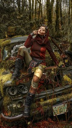 a woman sitting on top of an old car covered in mossy plants and trees