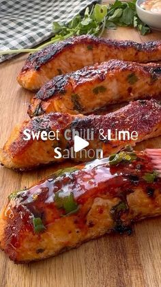 two pieces of meat sitting on top of a wooden cutting board next to a bowl of sauce