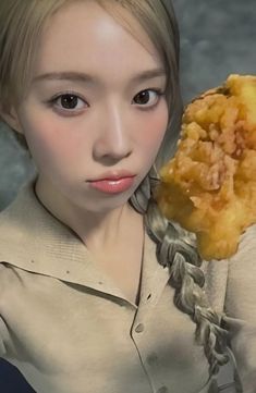 a woman holding up a fried food item in her right hand and looking at the camera