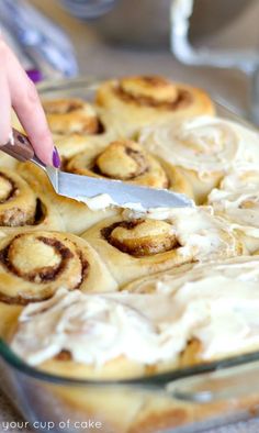 someone cutting into cinnamon rolls in a glass baking dish with icing on the top