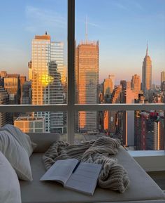 an open book is sitting on a couch in front of a window overlooking the city