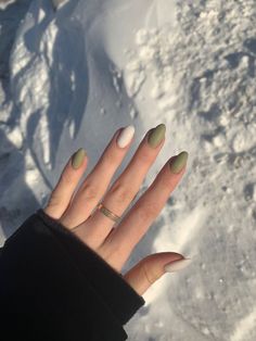 a woman's hand with green and white nail polish on it in the snow