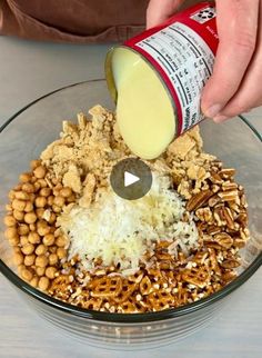 a person pouring dressing into a bowl filled with cereal, nuts and other food items